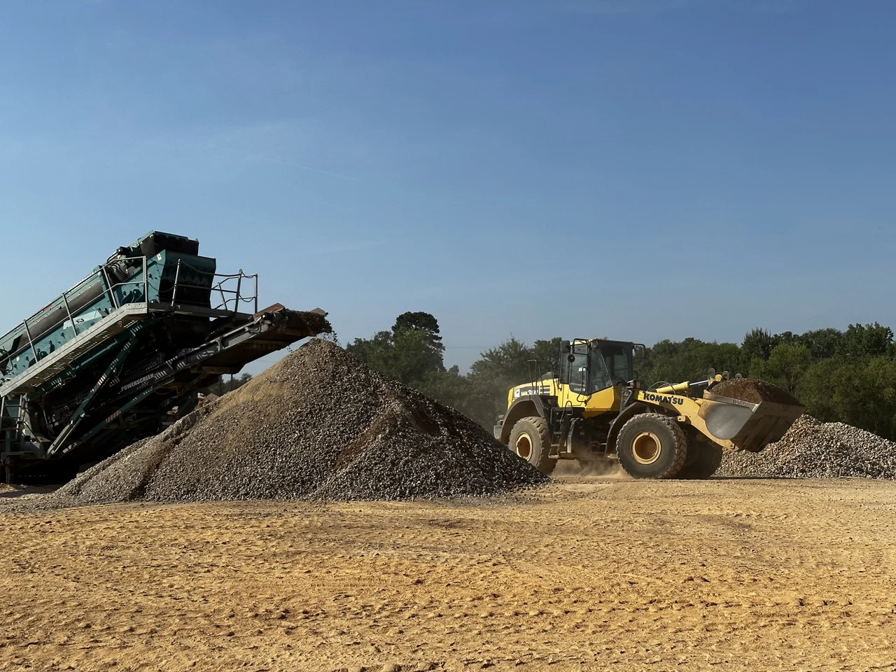 Wheel loader working beside crushed concrete processing equipment.